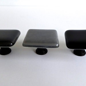 May include: Three square glass cabinet knobs with black metal bases. The knobs are in shades of gray and black.