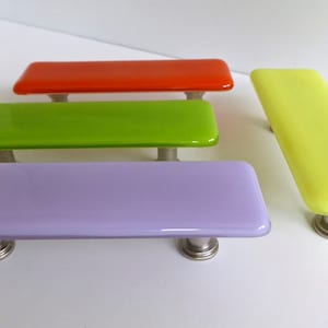 May include: Four glass cabinet knobs in different colours: orange, green, purple and yellow. Each knob has a silver metal base.