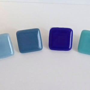 May include: Six square-shaped glass tiles in shades of blue, teal, and aqua. The tiles are arranged in a gradient from darkest blue to lightest aqua.