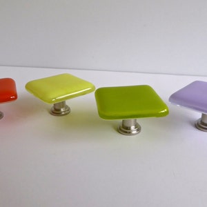 May include: Four square glass cabinet knobs with silver bases. The knobs are in shades of red, yellow, green, and purple.