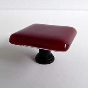 May include: A square-shaped glass cabinet knob with a dark red finish and a black metal base.