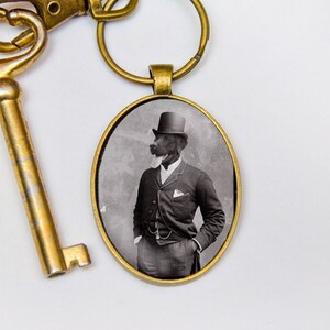May include: A gold-toned key chain with a round, black and white photo charm. The photo shows a dog wearing a top hat and a suit.