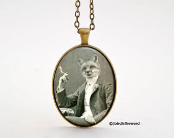 May include: A gold chain necklace with a round glass pendant featuring a black and white photo of a fox wearing a suit and holding a cigarette.
