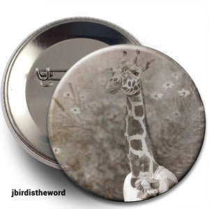May include: A vintage-style button featuring a black and white photograph of a giraffe's head and neck against a blurred background of foliage.