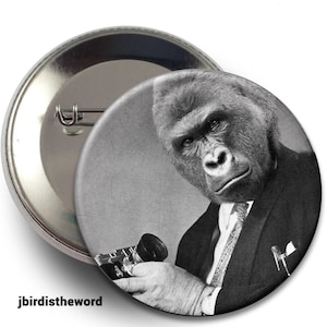 May include: A black and white photo of a gorilla wearing a suit and tie, holding a camera. The gorilla has a serious expression on its face.