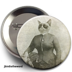 May include: A vintage-style button featuring a grumpy cat dressed in a Victorian-era gown. The cat has a serious expression and is holding a decorative object in its paw. The background is a faded, textured image.