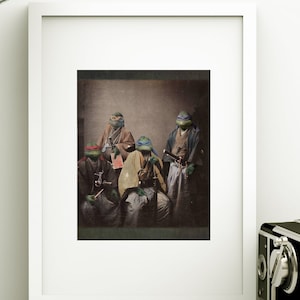 May include: A white rectangular picture frame containing a sepia-toned print of four anthropomorphic turtles dressed in traditional Japanese samurai attire, each wearing a colored eye mask, displayed alongside a silver desk lamp and a vintage camera.