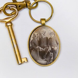 May include: A gold-toned key chain with a round, glass photo charm. The photo shows three dogs wearing hats and sitting together.