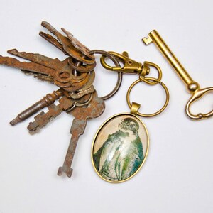 May include: A gold key chain with a variety of old keys and a round, glass charm with a vintage image of a woman.