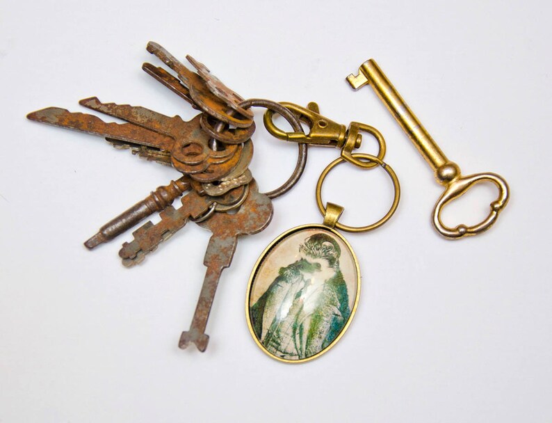 May include: A gold key chain with a variety of old keys and a round, glass charm with a vintage image of a woman.