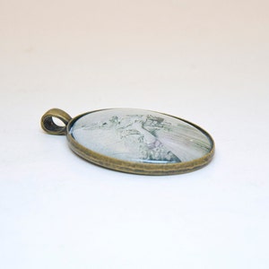 Op de afbeelding: Een bronzen ovale hanger met een wit en grijs beeld van een konijn dat een boeket bloemen vasthoudt.