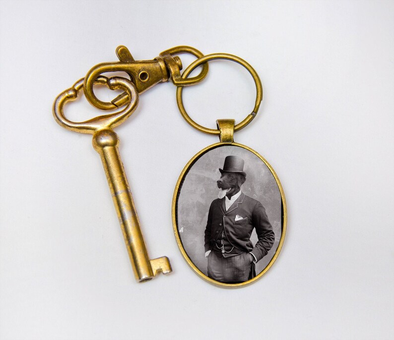 May include: A gold-toned key chain with a round, black and white photo charm. The photo shows a dog wearing a top hat and a suit.