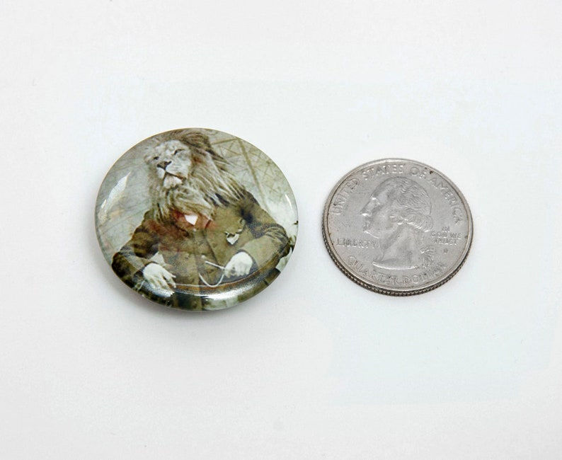 May include: A round button featuring a white lion in a suit, holding a pocket watch. The lion is seated in a chair. The button is approximately the size of a UK 20 pence coin.