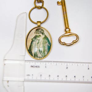 May include: A brass key chain with a round, oval-shaped charm featuring a vintage image of a person wearing a hat and coat. The charm is attached to a brass key ring. A separate brass skeleton key is also included.