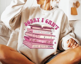 May include: A white sweatshirt with the text "Sorry I can't I have a date with my book boyfriend" in pink and a stack of pink books with flowers on them.