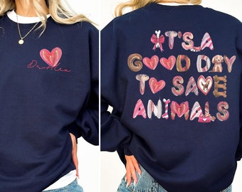 May include: Navy blue sweatshirt with a white crew neck collar. The front features a pink heart and the name "Dr. Alex" in cursive. The back displays the phrase "It's a good day to save animals" in a colorful, playful font.