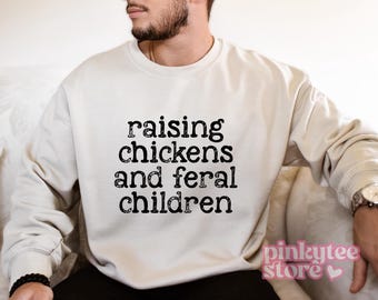 May include: A white sweatshirt with the text "raising chickens and feral children" printed in black.
