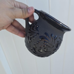 May include: Black ceramic mug with a floral design. The mug has a handle and a rounded body.