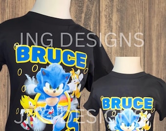 May include: Black t-shirt featuring a blue Sonic the Hedgehog character graphic, yellow rings, and the text "BRUCE BIRTHDAY BOY 5".