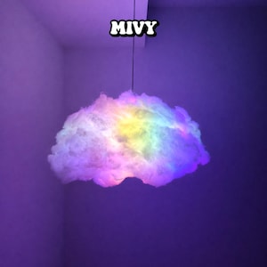 Puede incluir: Una lámpara colgante con forma de nube con un degradado de colores arcoíris. La luz está suspendida de un cable negro y tiene la palabra "MIVY" en texto blanco en la parte superior.