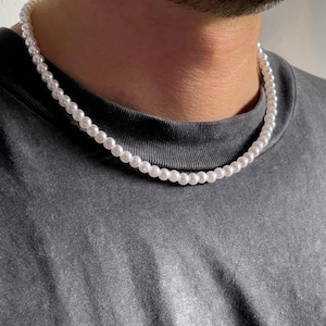 Op de afbeelding: Een witte parelketting gedragen om de nek van een persoon. De ketting is gemaakt van kleine, ronde parels en is ongeveer 45 cm lang.