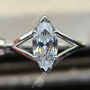 Könnte beinhalten: Ein Ring mit einem Diamanten im Marquiseschliff und einem silbernen Band. Der Diamant ist in einem geometrischen Design gefasst und hat ein klares, funkelndes Aussehen. Der Ring ist eine Nahaufnahme, die die Details des Schmucks hervorhebt.