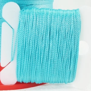 May include: A spool of turquoise blue thread wound around a white plastic bobbin. The thread is smooth and appears to be made of a synthetic material.