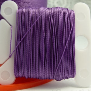 May include: A spool of purple thread wound around a white plastic thread holder.