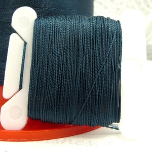 May include: A spool of dark blue thread wound around a white plastic thread holder.