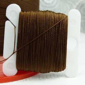 May include: A spool of brown embroidery floss wound around a white plastic thread holder.