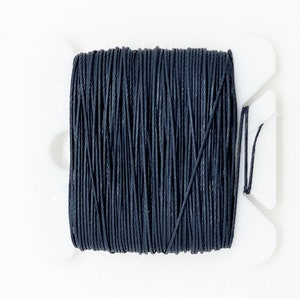 May include: A spool of black waxed cotton cord, wound on a white plastic bobbin.