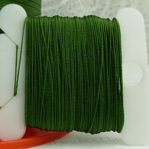 May include: A spool of dark green thread wound around a white plastic bobbin. The thread is smooth and appears to be made of cotton.