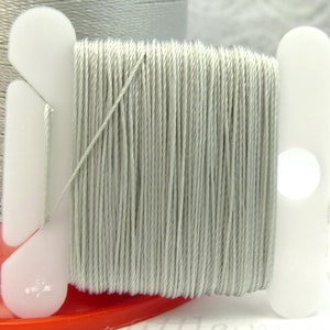 May include: A spool of light gray thread wound on a white plastic bobbin. The thread is smooth and appears to be made of cotton.