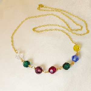 May include: A gold chain necklace with a rainbow of crystal beads. The beads are clear, green, burgundy, yellow, and blue.