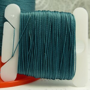 May include: Teal colored thread wound on a white plastic spool. The thread is wound tightly and evenly.