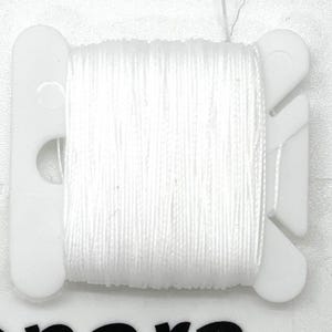 May include: A spool of white thread wound around a white plastic bobbin.