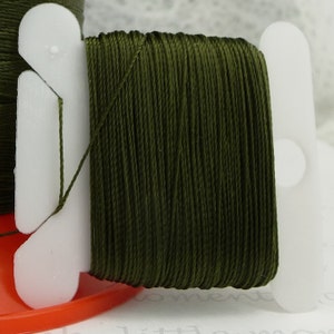 May include: A spool of dark green thread wound on a white plastic bobbin.