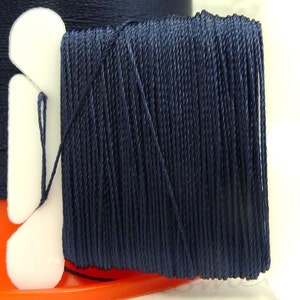 May include: A spool of dark blue thread wound around a white plastic bobbin. The thread is tightly wound and has a smooth, even texture.