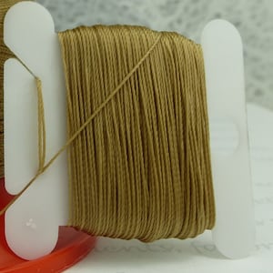 May include: A spool of brown embroidery floss wound on a white plastic bobbin.