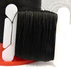 May include: A spool of black thread wound around a white plastic bobbin. The thread is tightly wound and appears to be made of a fine, smooth material.