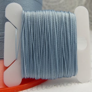 Puede incluir: Una bobina de hilo de bordar azul claro enrollado en una bobina de plástico. El hilo está listo para ser utilizado para coser o proyectos de artesanía.