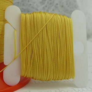 May include: A spool of bright yellow thread wound around a white plastic thread holder.