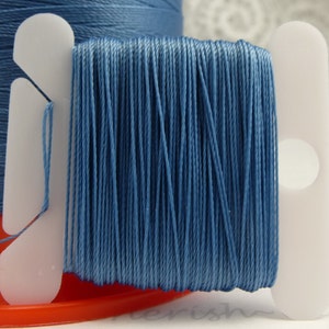 May include: A spool of light blue thread wound on a white plastic bobbin. The thread is wound tightly and evenly, and the bobbin has a small hole in the centre.