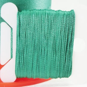 Peut inclure: Une bobine de fil vert sarcelle enroulée autour d'une bobine en plastique blanche. Le fil est enroulé serré et semble être fait d'un matériau fin et lisse.