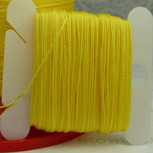 May include: A spool of bright yellow thread wound around a white plastic bobbin. The thread is held in place by a white plastic clip.