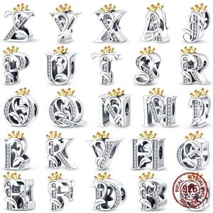 May include: A selection of silver alphabet charms, each adorned with a gold crown. The charms showcase detailed floral patterns and are decorated with tiny, sparkling stones. A silver charm with a "925" stamp is also visible.
