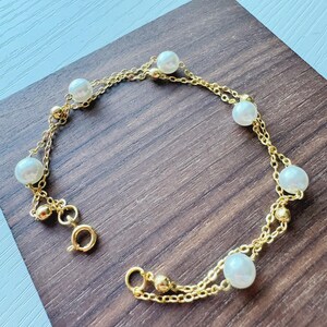 Può includere: Un braccialetto a catena dorata con perle bianche. Il braccialetto ha una chiusura a moschettone.