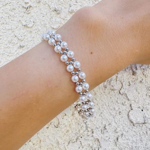 Puede incluir: Un brazalete de doble fila de perlas blancas y cuentas plateadas.