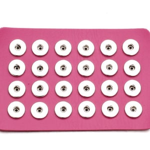 May include: A pink sheet with 24 silver snap buttons arranged in a grid pattern.