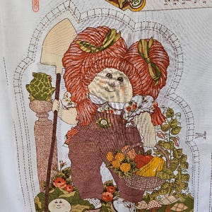 May include: A vintage Cabbage Patch Kids fabric panel featuring a doll with red hair, overalls, and a basket of produce. The doll is holding a shovel. The panel includes instructions and a decorative border.